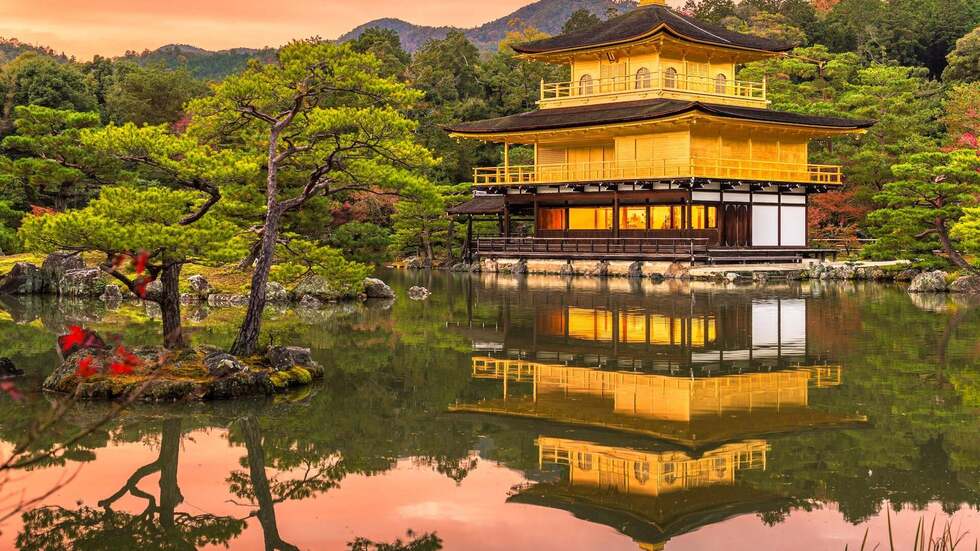 Golden temple reflecting on a calm lake surrounded by trees at sunset.